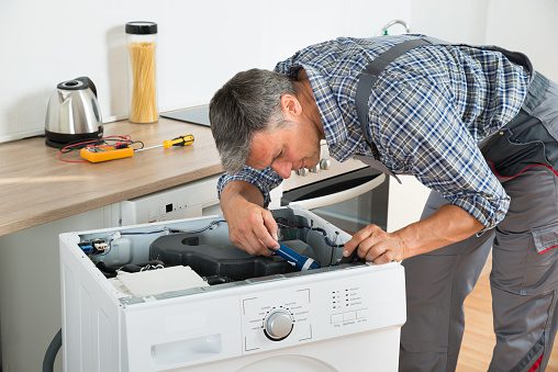 handyman checking washing machine with flashlight in kitchen